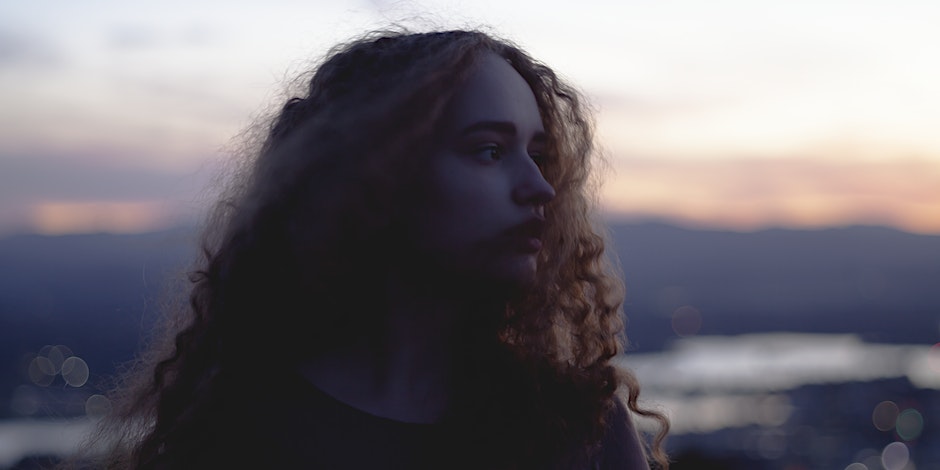 Photo of girl with curly hair looking to her left with landscape in the background.