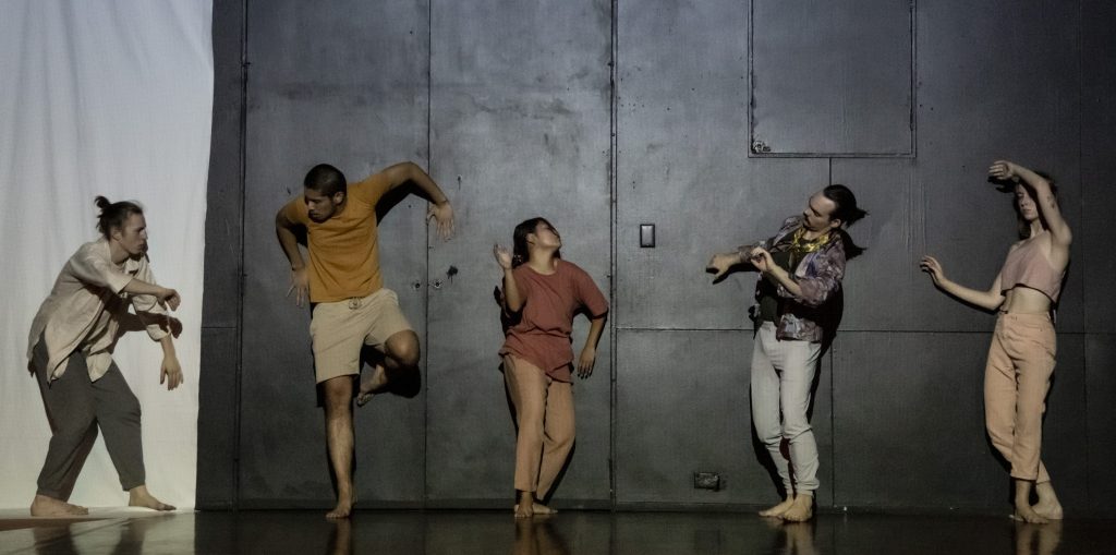 Five dancers pose in a line across a wall.