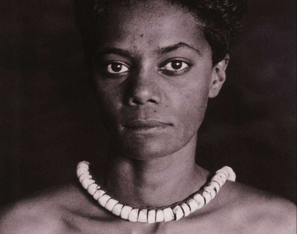A black and white image of a woman wearing a beaded necklace.