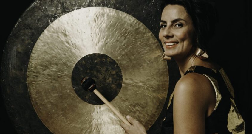 Woman standing next to a large percussion instrument. She is looking at us and smiling.