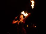 The artist Jazida is twirling fire on stage. They are wearing a corset with dramatic makeup.