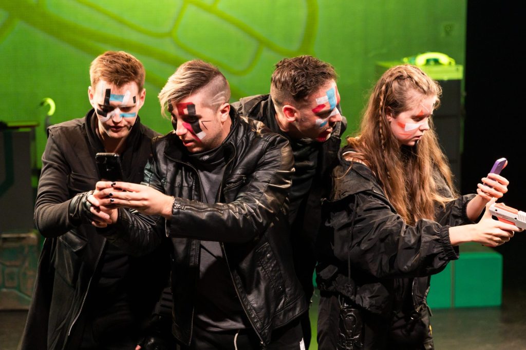 The cast of I have no enemies are lined up on stage and looking intensely at their phones.