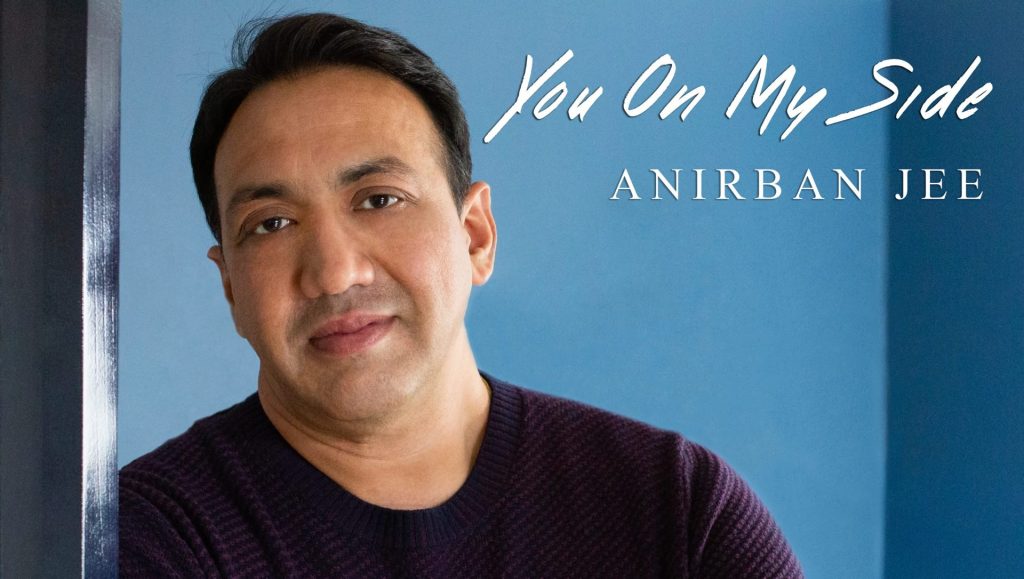 A photo of Anirban Jee's single cover. He is leaning against a blue wall and smiling
